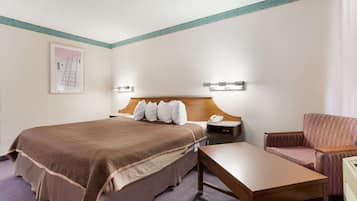 A hotel room with a large bed, a wooden headboard, a nightstand, a desk, a chair, and a framed picture on the wall.