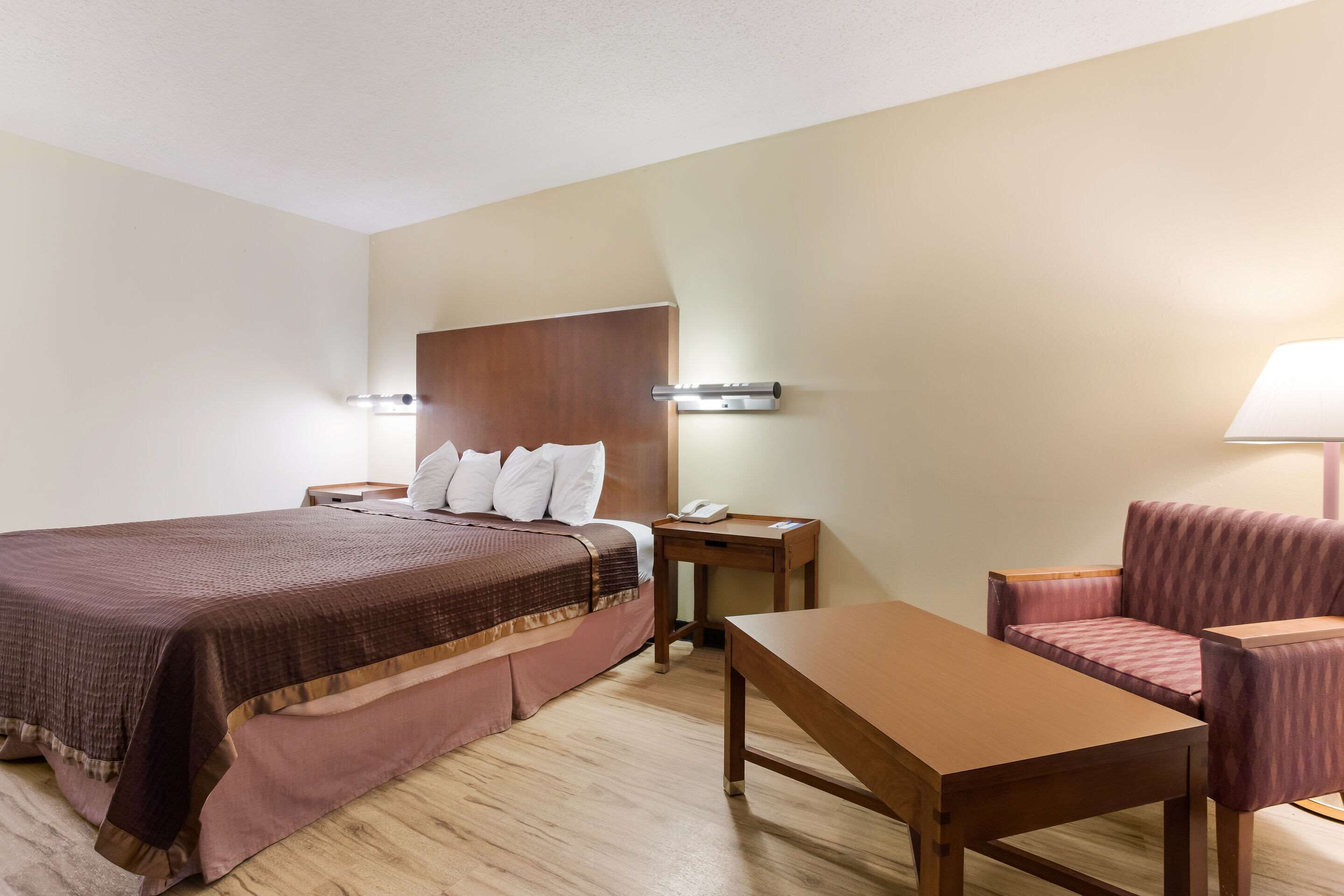 Une chambre d’hôtel avec un lit, une table de chevet, une lampe et un petit canapé.