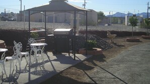 Un espace extérieur abrité, aménagé avec un barbecue, des chaises en métal blanc et une structure en forme de tente.