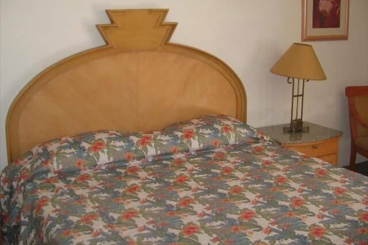 Un lit avec une couvre-lit à motifs floraux, une tête de lit en bois et une table de chevet avec une lampe.