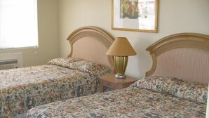 Une chambre avec deux lits, chacun agrémenté de draps à motifs floraux, une table de chevet avec une lampe et un tableau encadré au mur.