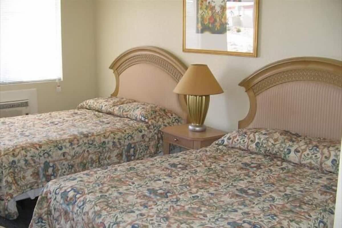 Une chambre avec deux lits, chacun agrémenté de draps à motifs floraux, une table de chevet avec une lampe et un tableau encadré au mur.