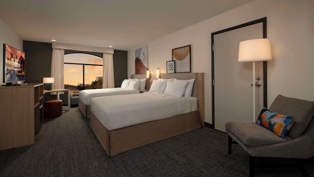 A hotel room with two beds, a desk, a chair, a TV, and a view of the sunset. - Spark by Hilton Houston Bush Intercontinental Airport (Houston)