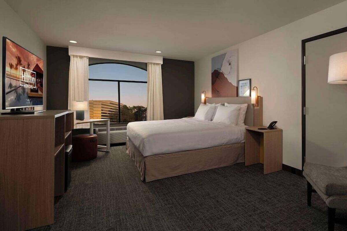 A hotel room with a bed, a desk, a chair, a TV, and a window with a view.