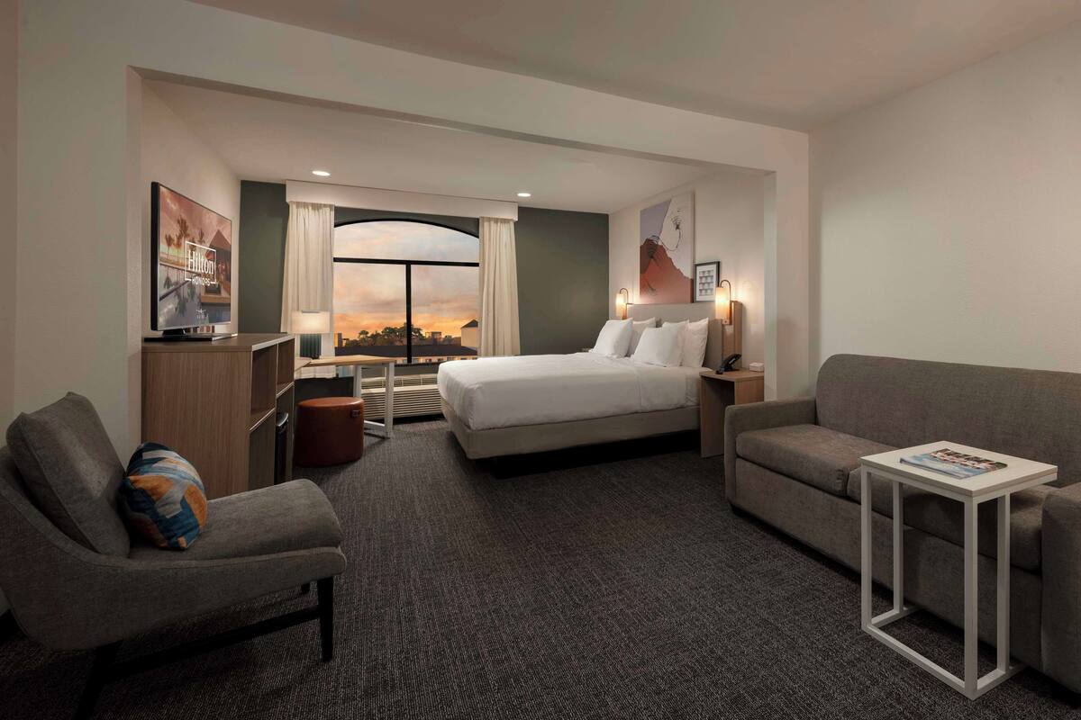 A hotel room with a bed, a sofa, a desk, and a TV.
