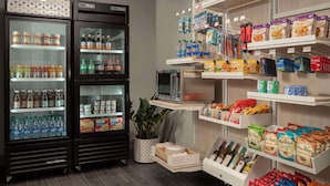 A kitchenette area with a refrigerator stocked with beverages, a microwave, and various food items on shelves. - Spark by Hilton Houston Bush Intercontinental Airport (Houston)