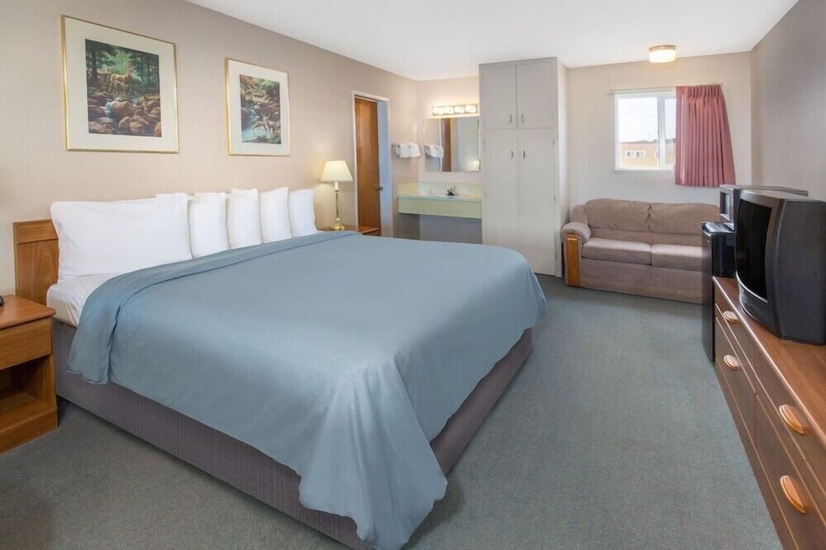 A hotel room with a large bed, a sofa, a TV, a dresser, a mirror, and framed pictures on the wall.