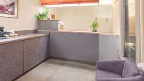 Zona de recepción con mostrador, máquina de café y un espacio de espera con una silla morada.