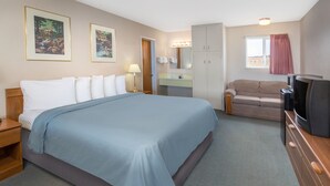 Habitación de hotel con una cama grande, un sofá, un televisor, un aparador, un espejo y una ventana con cortinas.