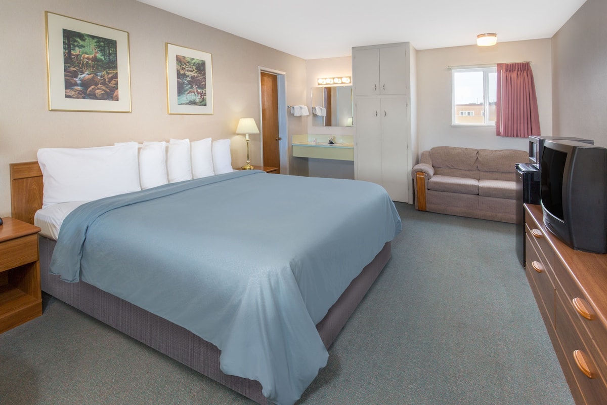 A hotel room with a large bed, a sofa, a TV, a dresser, a mirror, and a window with curtains.