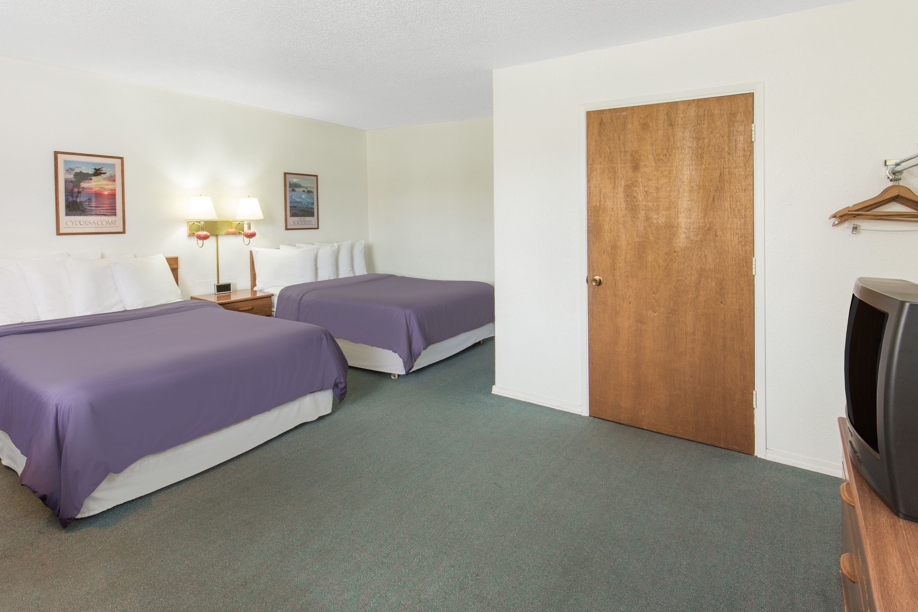 Habitación de hotel con dos camas, una puerta de madera, un televisor y dos lámparas fijadas a la pared.