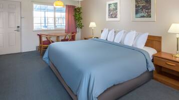 A hotel room with a large bed, a desk with a chair, a window with curtains, and two wall-mounted lamps.