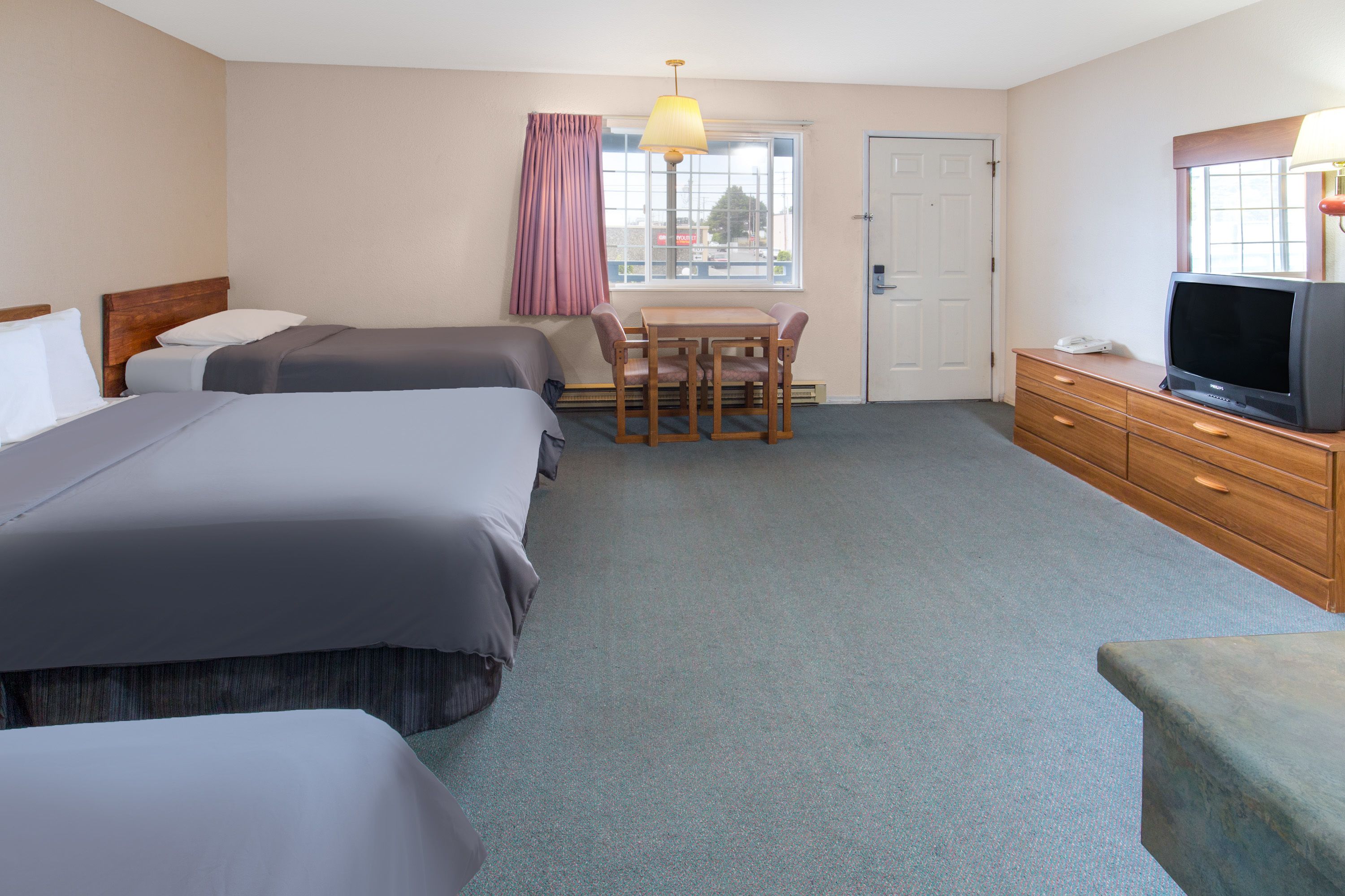 Une chambre d’hôtel avec deux lits, une petite table avec des chaises, un téléviseur et une commode.
