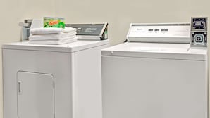 Two white front-loading washers stacked on top of each other with a Gain detergent box and a Whirlpool instruction manual on the top washer. - Travelodge by Wyndham St. Louis (St. Louis)