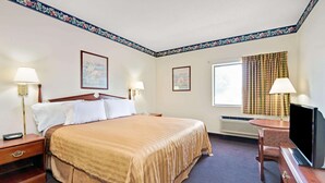 A hotel room with a large bed, two bedside tables, a TV, a desk, and a window with curtains. - Travelodge by Wyndham St. Louis (St. Louis)