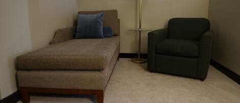 A small, neatly arranged bedroom with a bed, a chair, and a floor lamp.