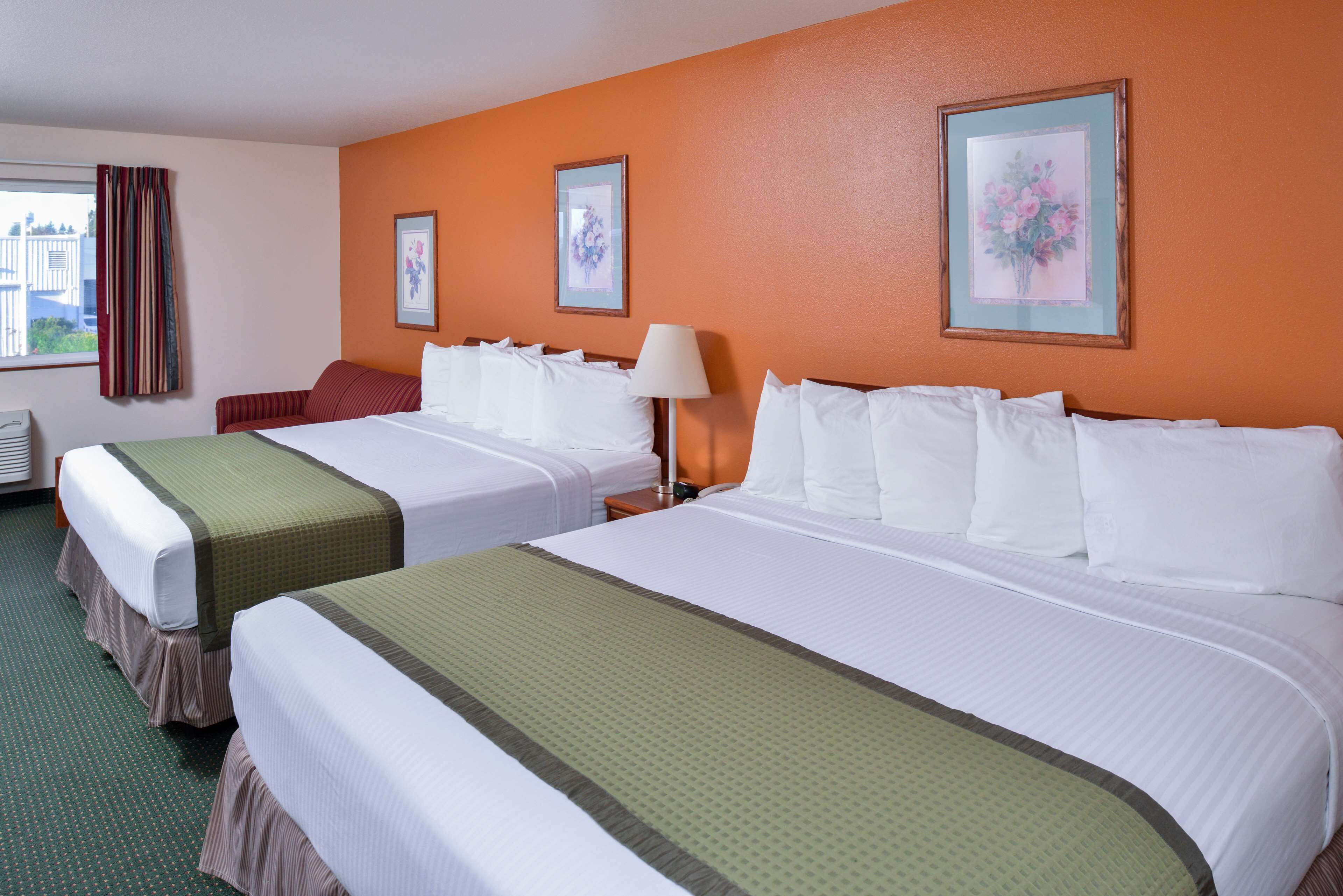 Een hotelkamer met twee bedden, een raam met gordijnen en twee ingelijste foto's aan de muur.