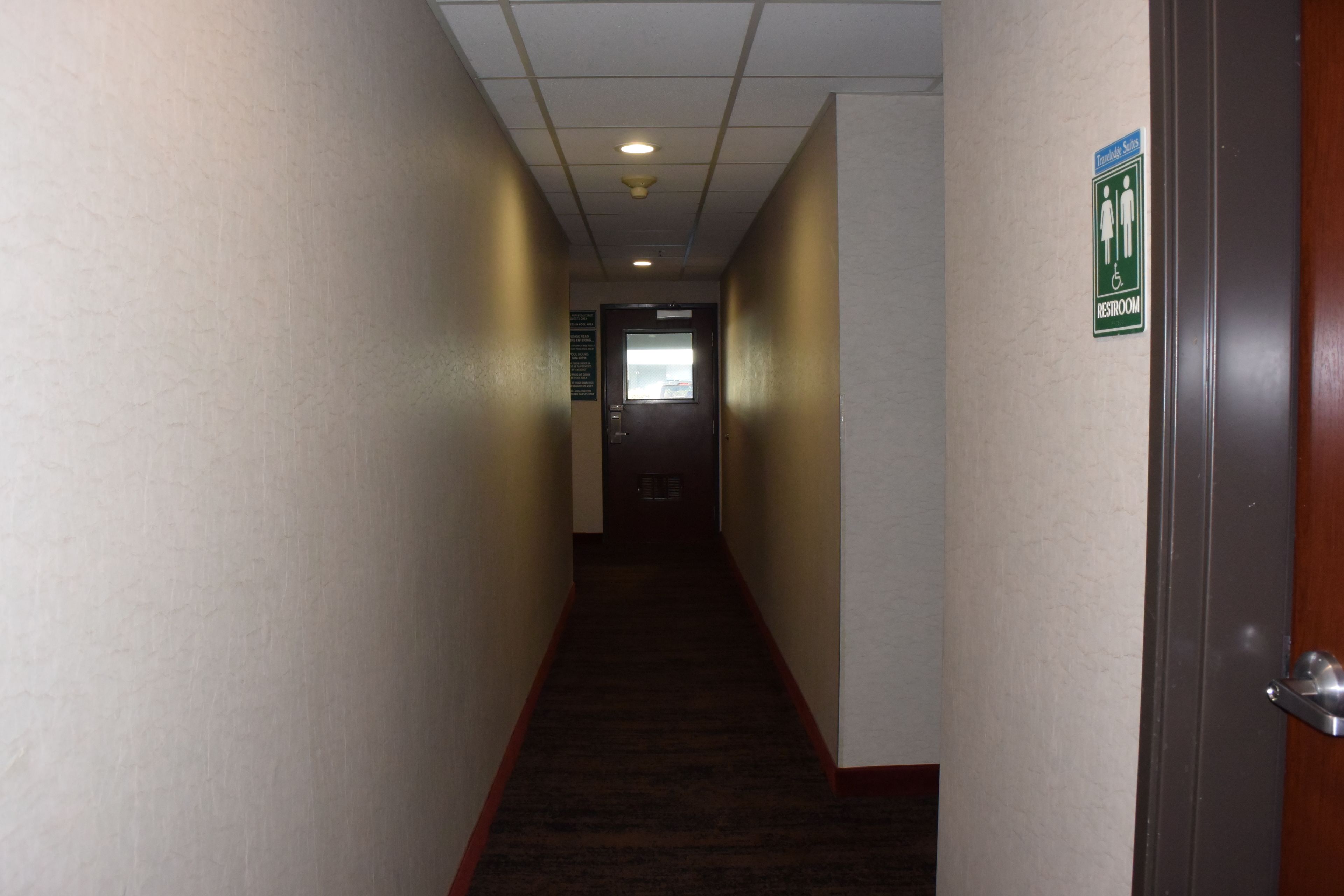 A narrow hallway with a carpeted floor, a door on the right, and a sign indicating a men's restroom.