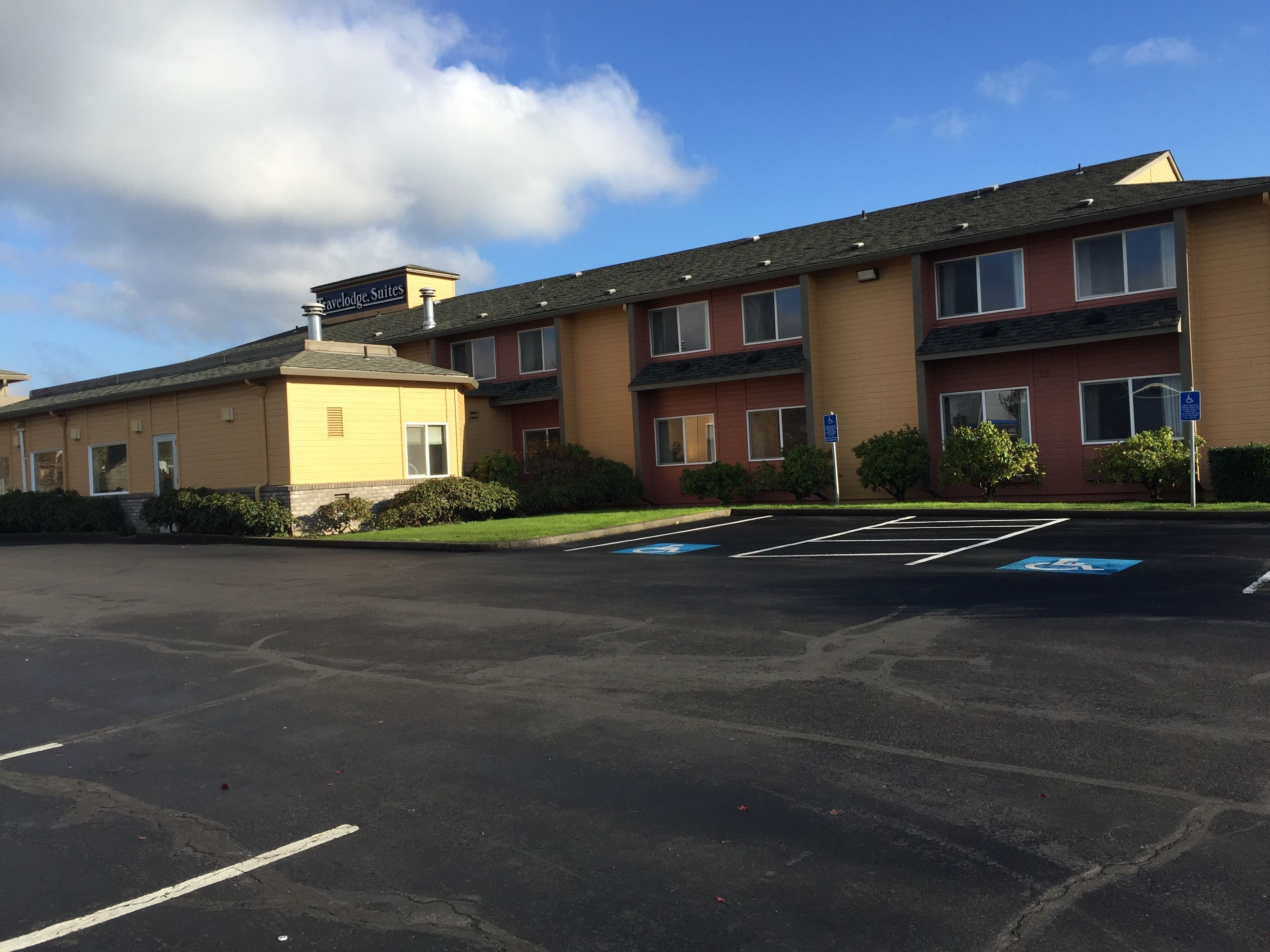 A hotel with a yellow exterior, multiple windows, and a parking lot with handicapped parking spaces.
