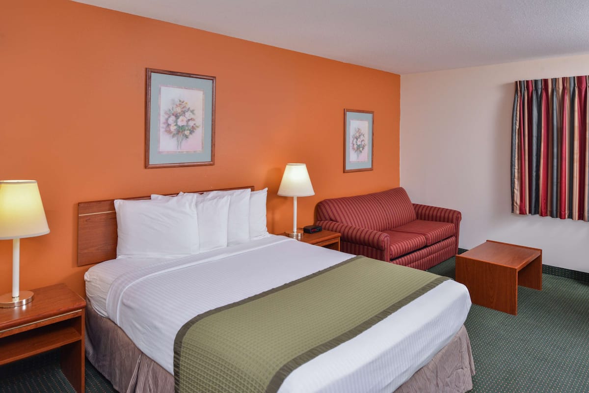 Ein Hotelzimmer mit einem Bett, zwei Nachttischen, einem Sessel und zwei gerahmten Bildern an der Wand.