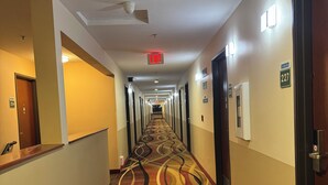 Un couloir d’hôtel avec un tapis à motifs, des portes et un panneau indiquant la sortie.