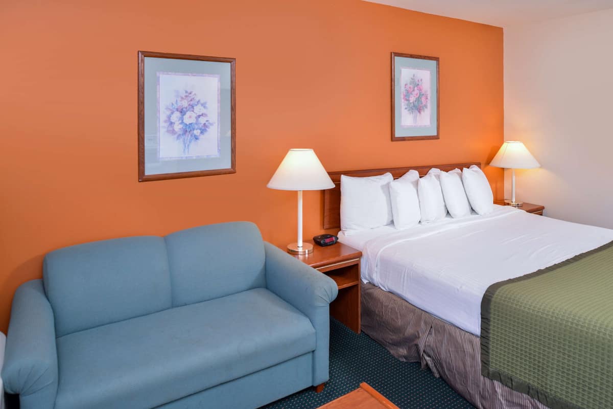 Ein Hotelzimmer mit einem blauen Sofa, einem Bett mit weißer Bettwäsche, zwei gerahmten floralen Bildern an der Wand und zwei Nachttischlampen.