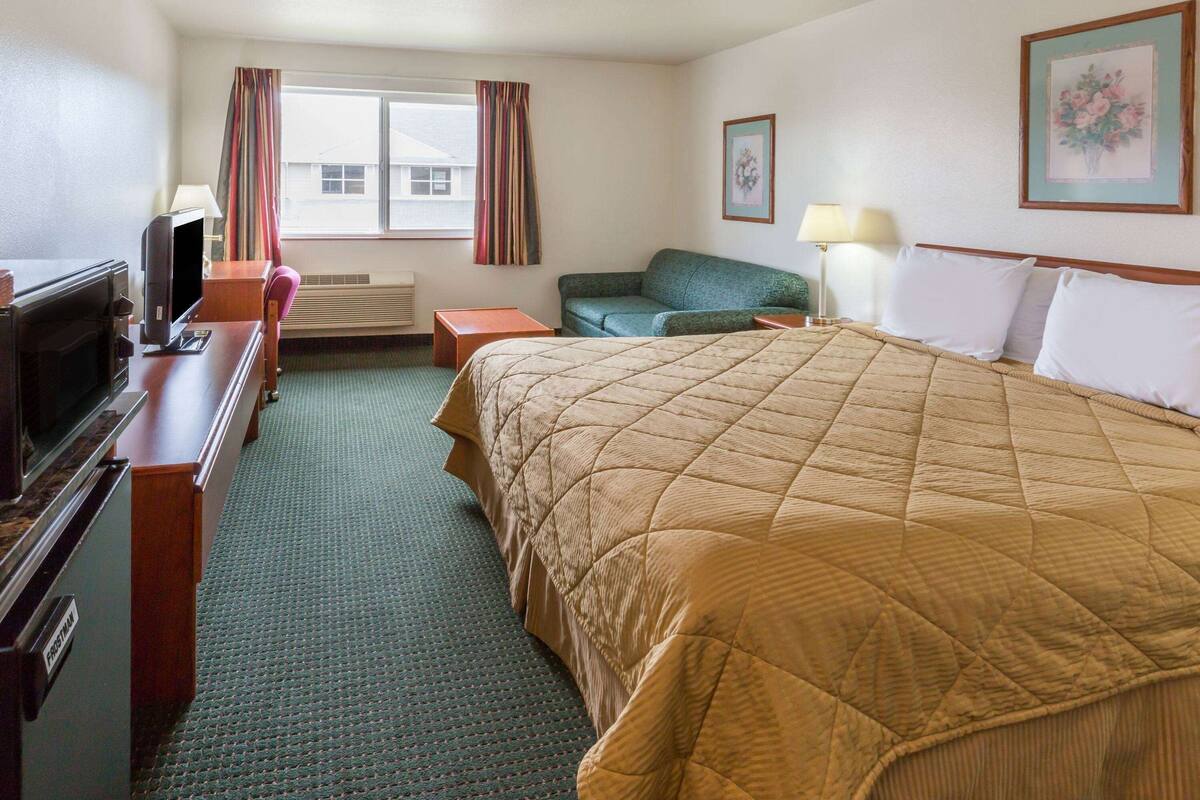 Ein Hotelzimmer mit Bett, Schreibtisch mit Fernseher, einer Couch und einem Fenster mit Vorhängen.