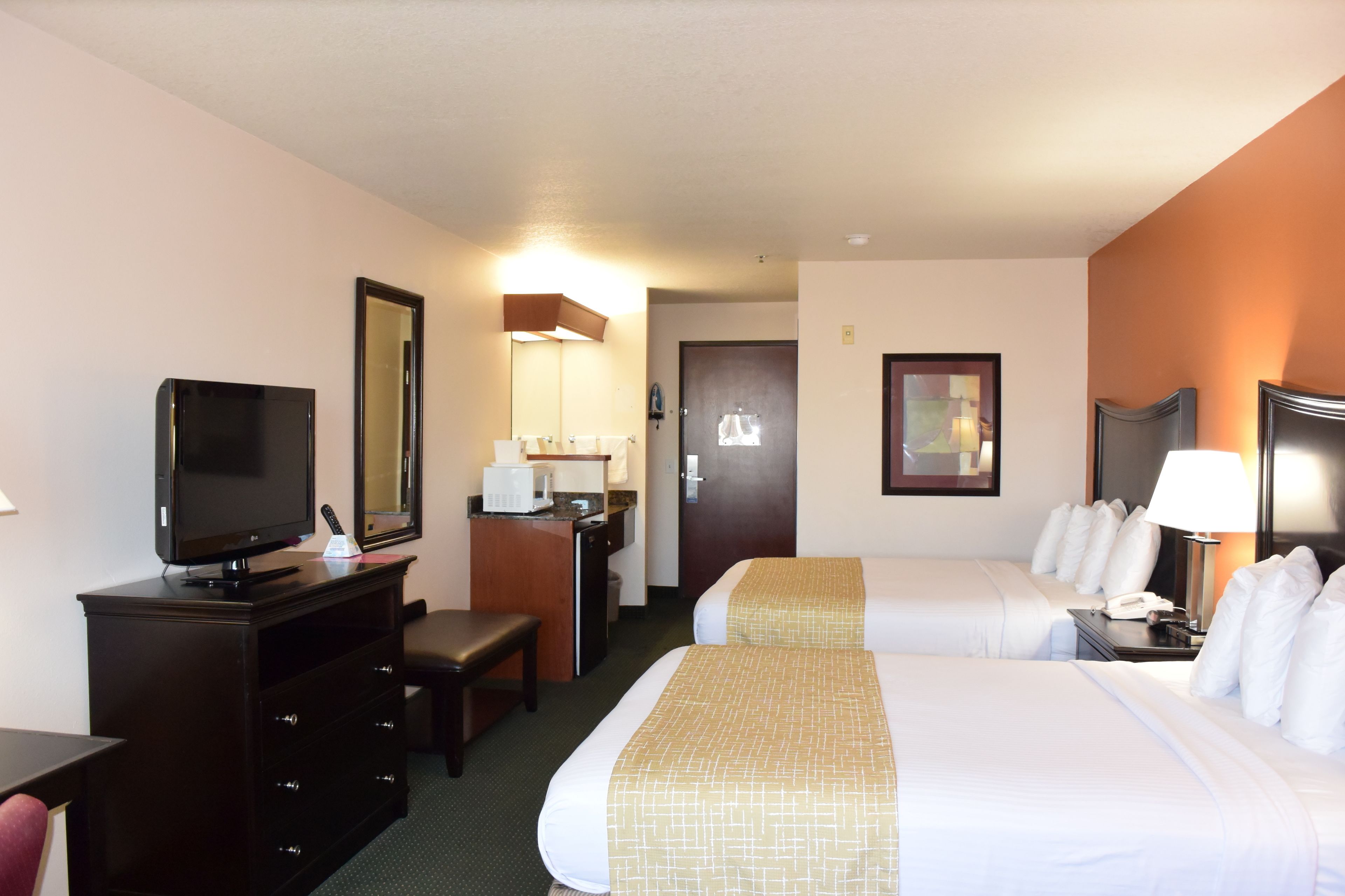 Una habitación de hotel con cama, escritorio, televisión, lámpara de escritorio, silla y puerta.