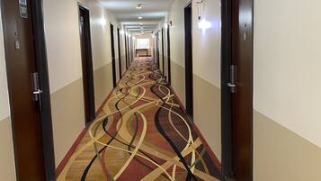Un couloir d’hôtel avec un tapis à motifs, de nombreuses portes et un luminaire au plafond.