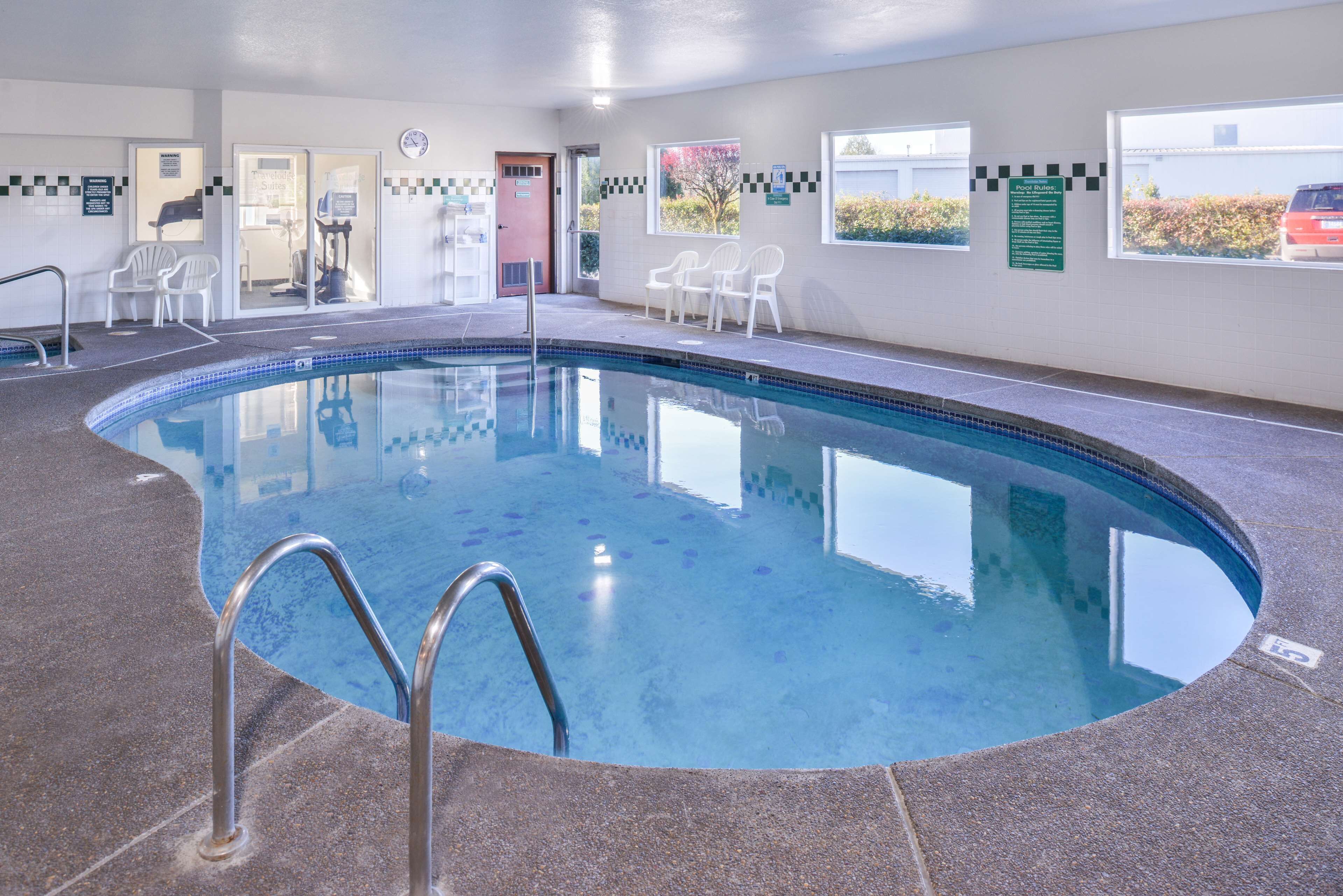 Piscina interna com água cristalina, piso ladrilhado e algumas cadeiras próximas.