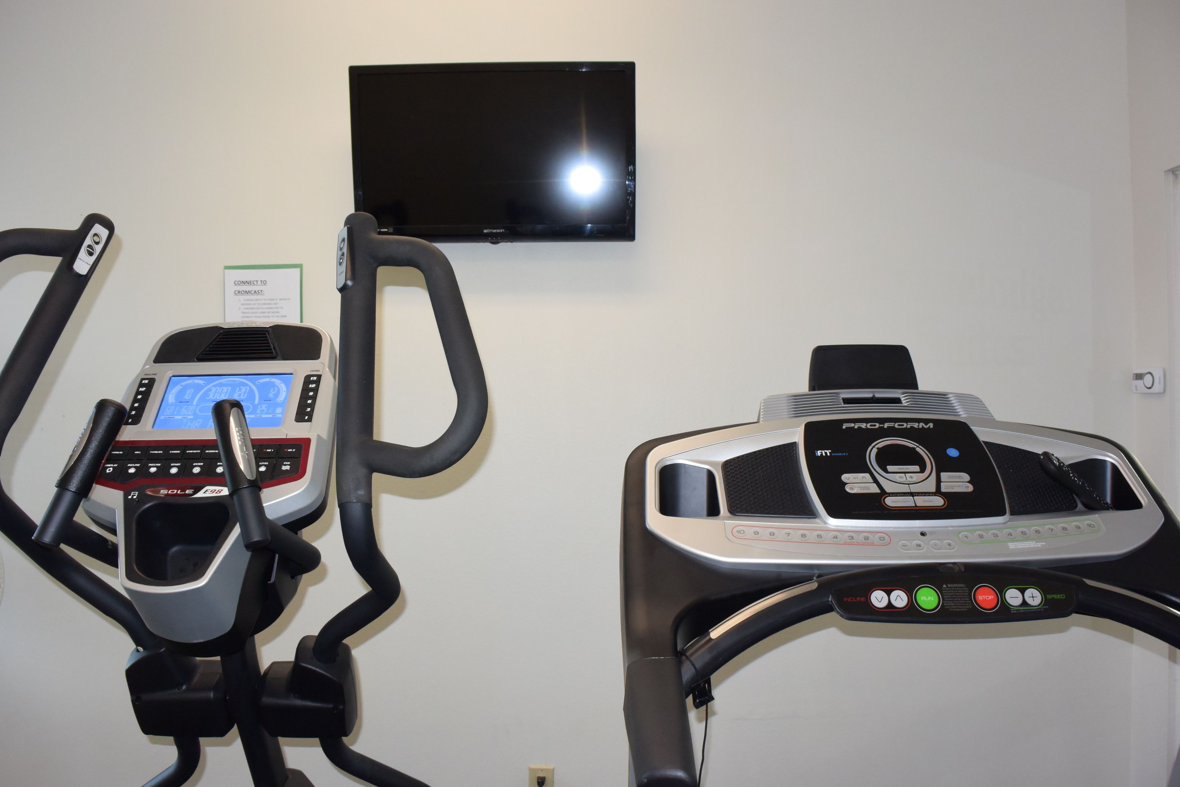 Dos bicicletas estáticas con pantallas digitales y un televisor montado en la pared.
