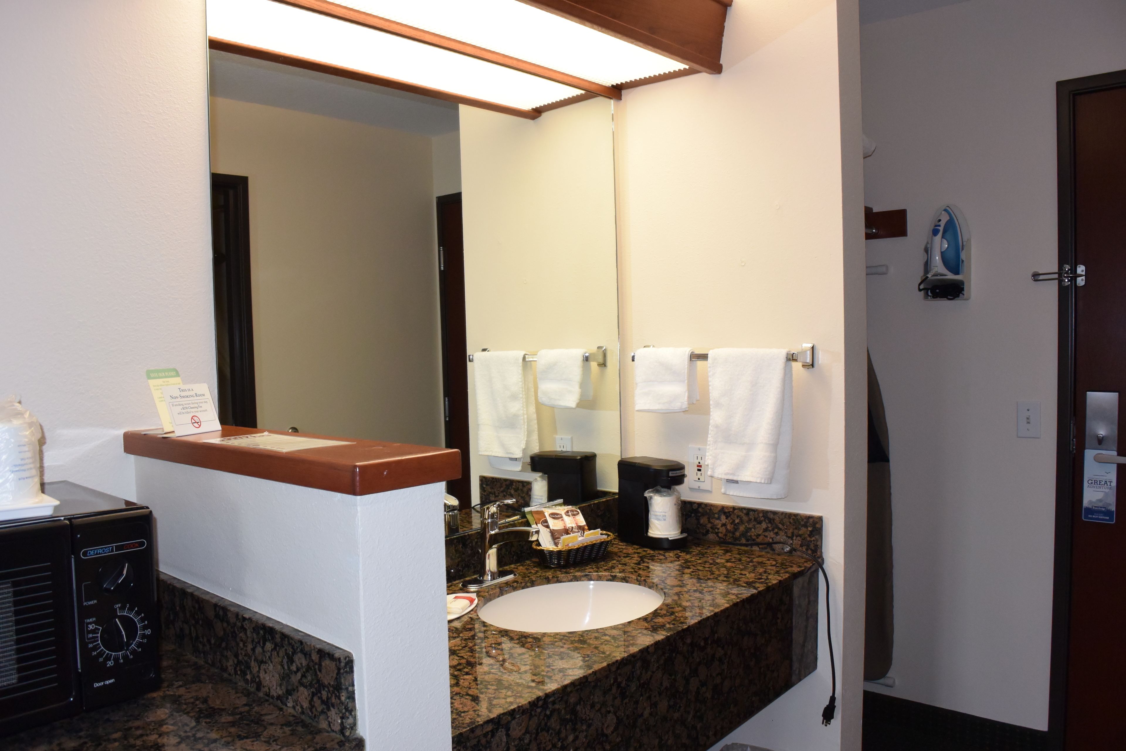 A hotel bathroom with a granite countertop sink, a mirror, a towel rack, and a coffee maker.