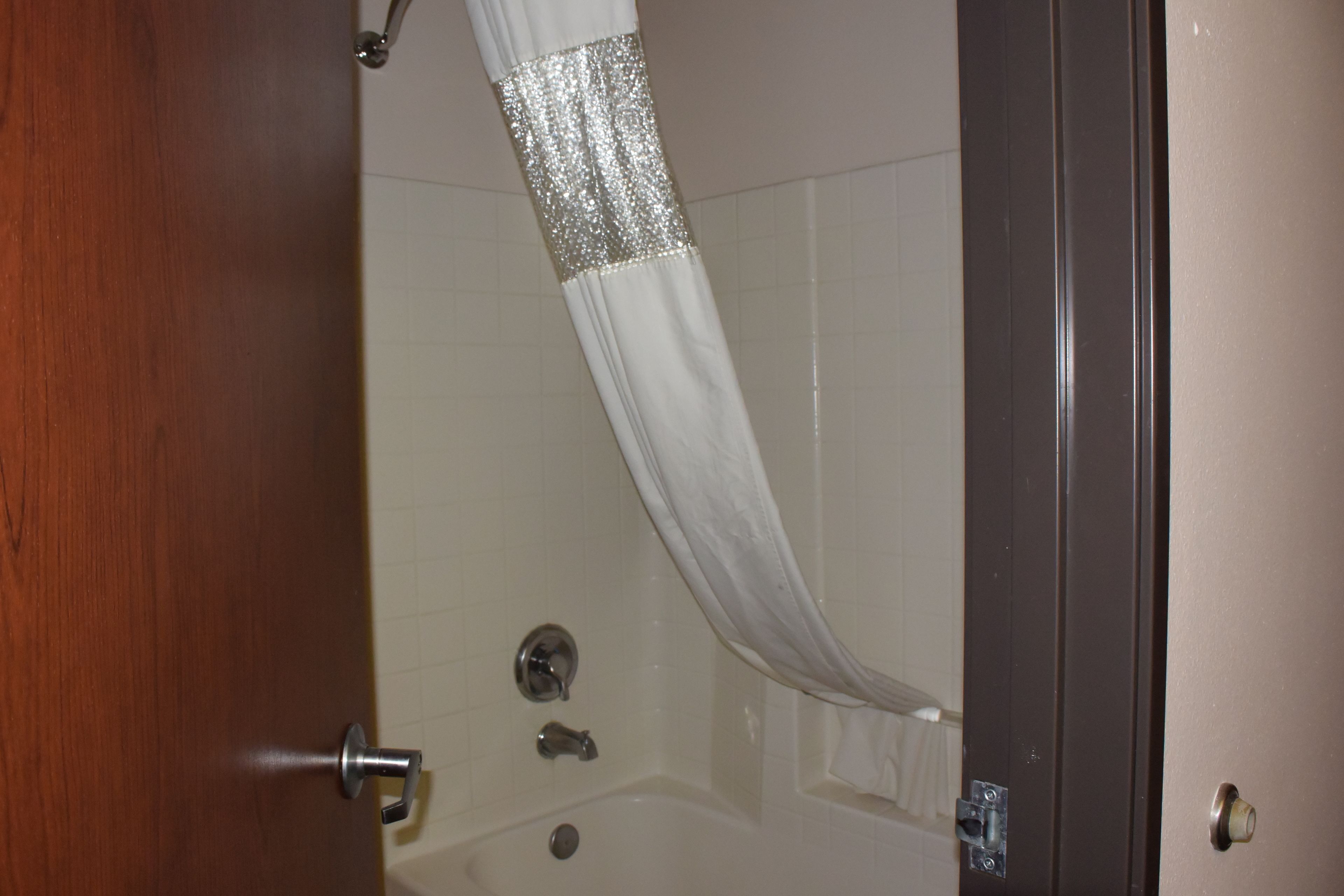 A bathroom with a white shower curtain, a bathtub, and a wooden door.