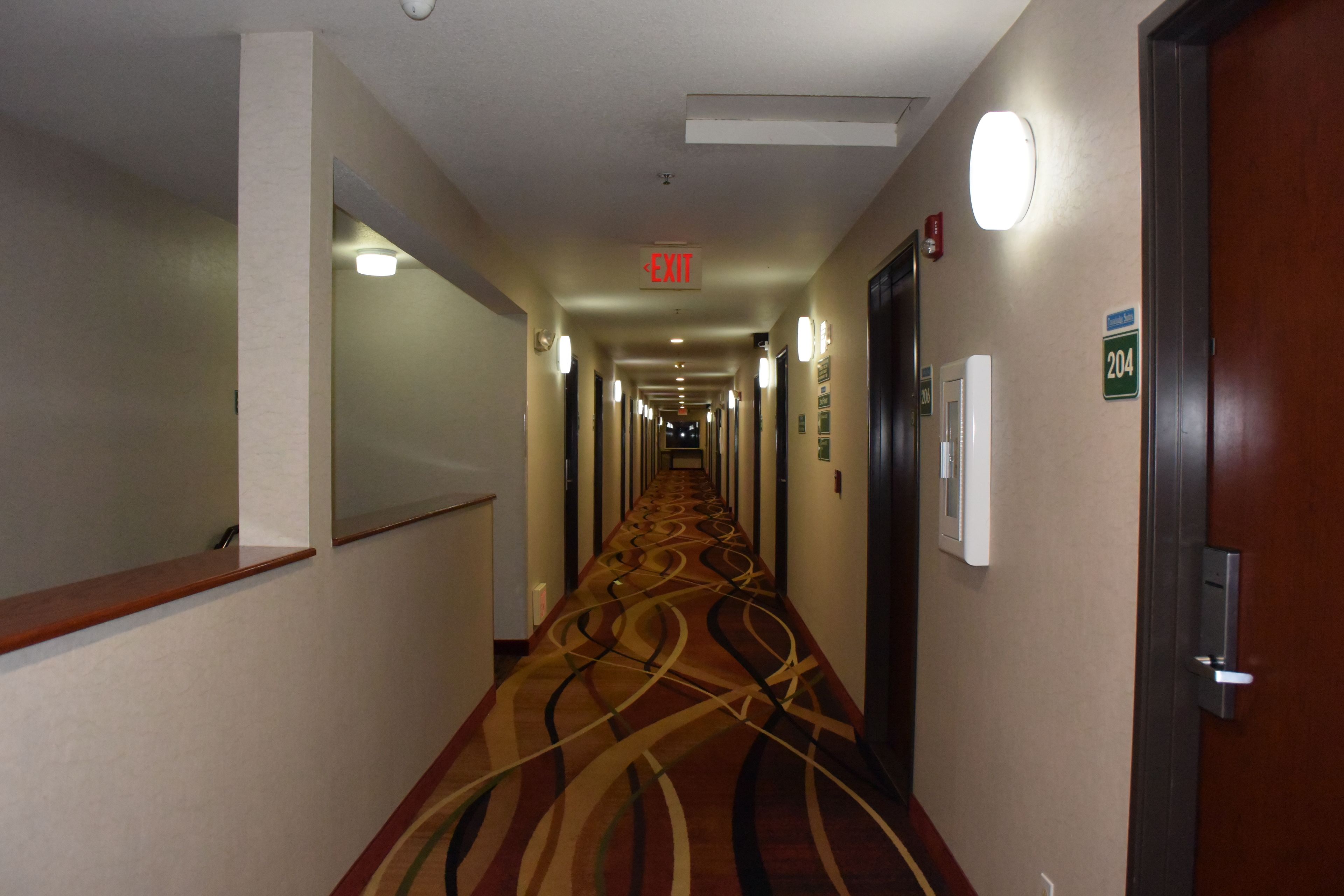 A hotel hallway with a carpeted floor, an exit sign, and a door with a number sign.