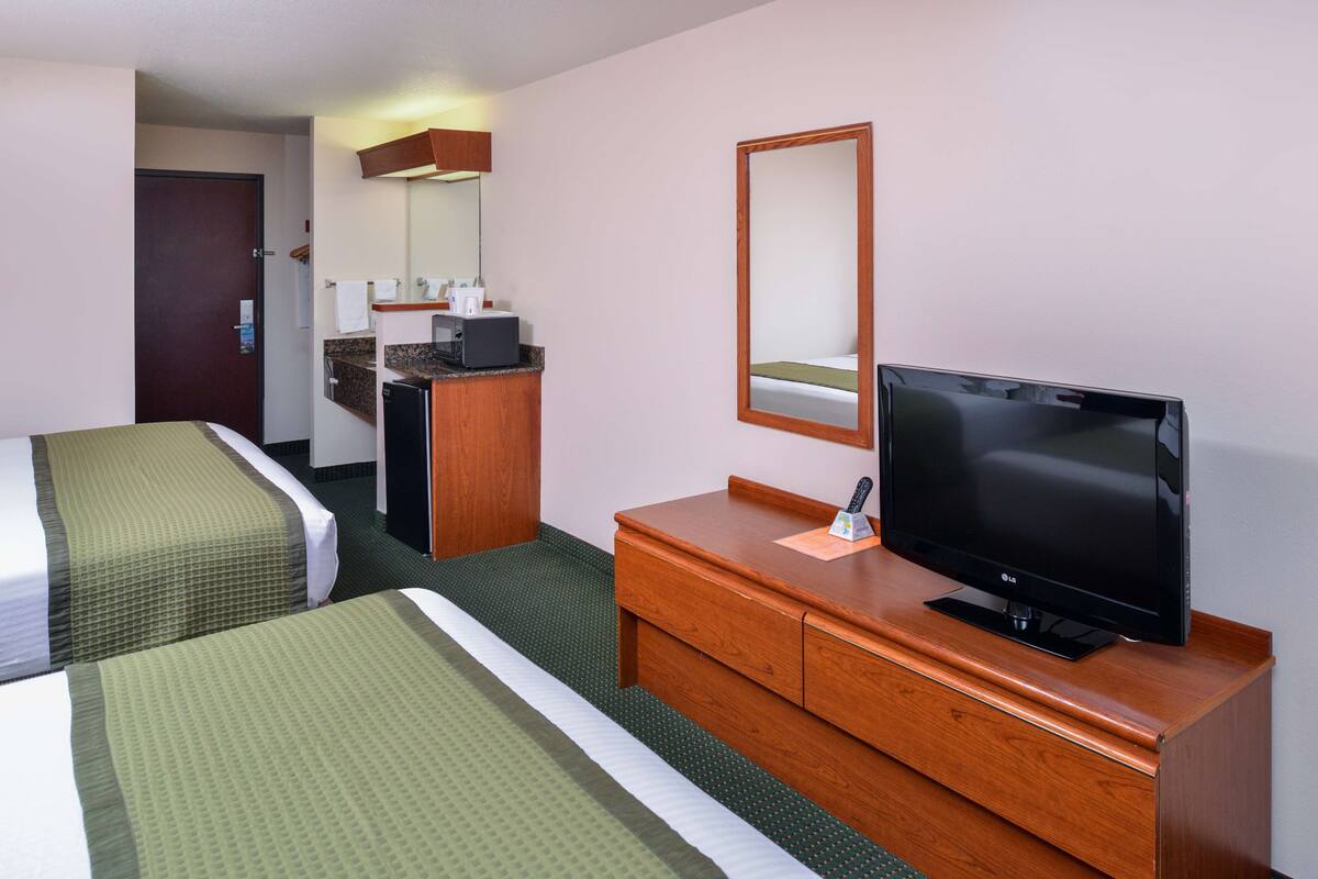 Ein Hotelzimmer mit zwei Betten, einem hölzernen Schminktisch, einem Fernseher und einem Spiegel.
