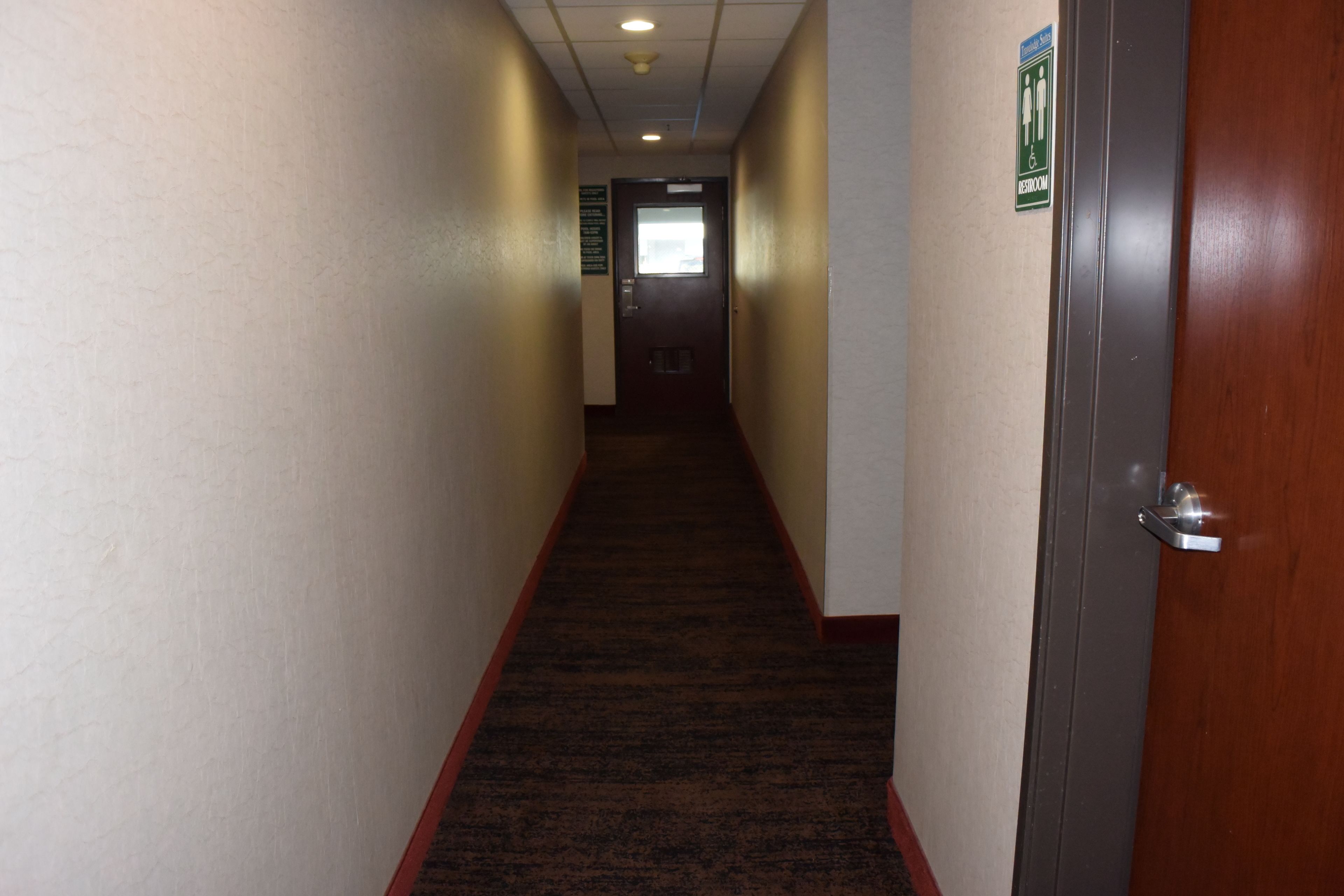 A hallway with a carpeted floor, a door on the right, and a sign on the wall.