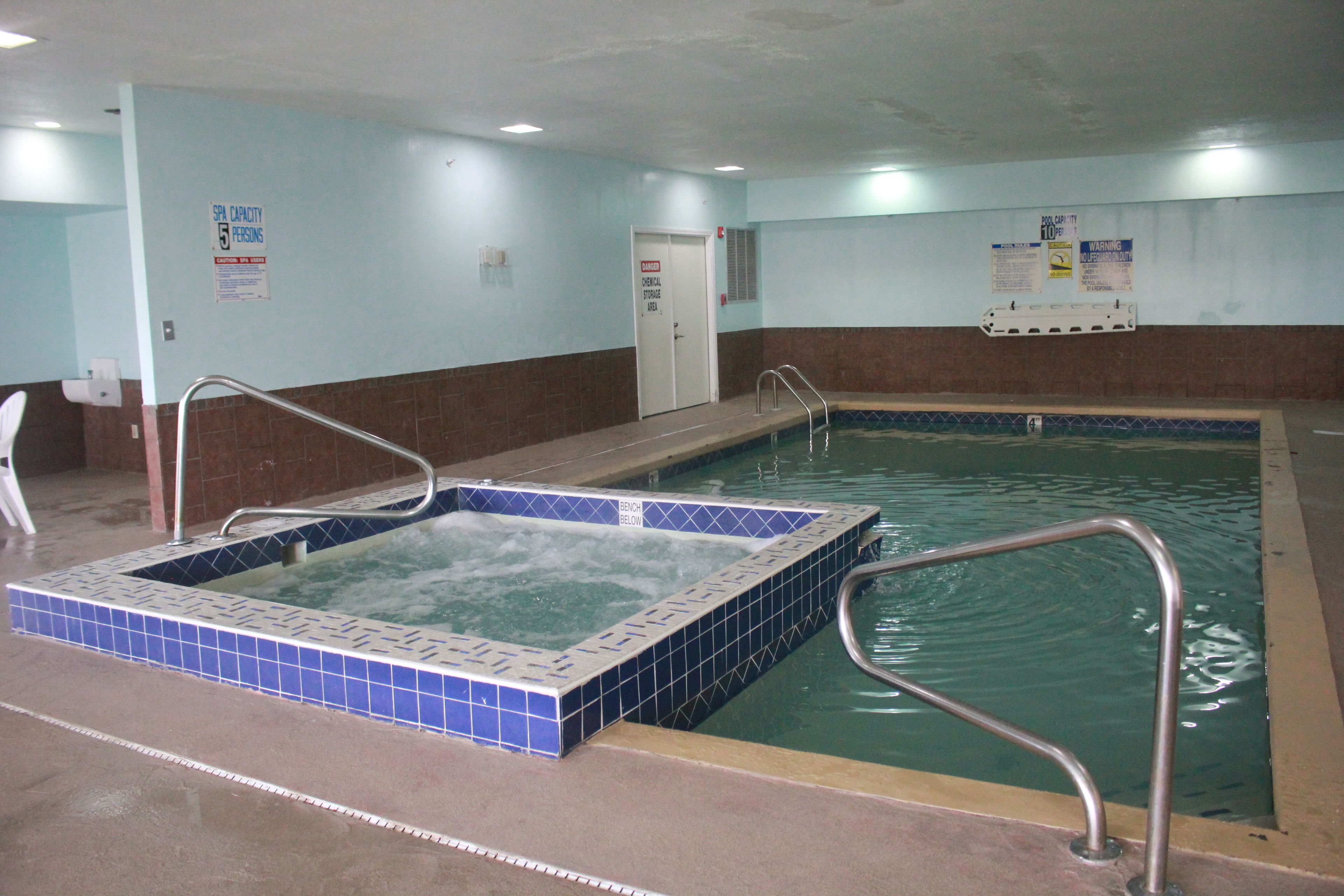 En inomhuspool med bubbelbad, metallräcken och kaklade väggar.