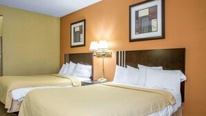A hotel room with two beds, a nightstand with a lamp, and framed artwork on the walls.
