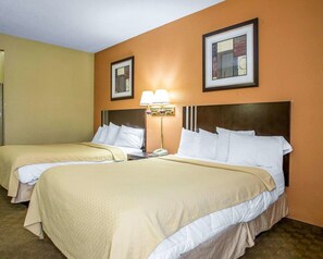 A hotel room with two beds, a nightstand with a lamp, and framed artwork on the walls.