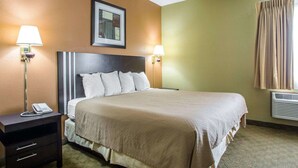 A hotel room with a large bed, two bedside lamps, a nightstand with a phone, a framed picture on the wall, and a window with curtains.