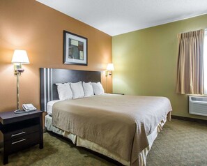 A hotel room with a large bed, two bedside lamps, a nightstand with a phone, a framed picture on the wall, and a window with curtains.