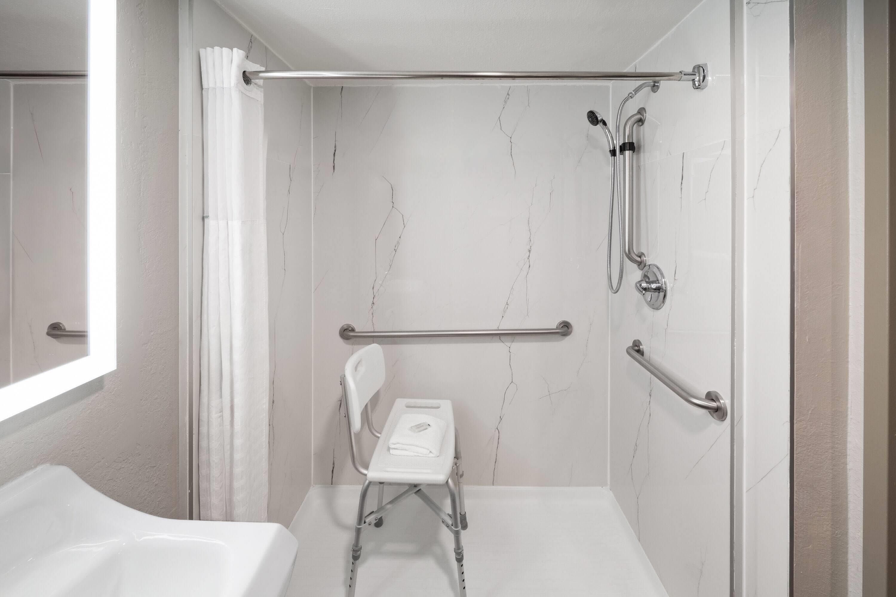 Ett badrum med dusch, stödhandtag, en bänk som är anpassad för rullstolar och ett badkar.