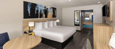 A hotel room with a bed, bedside table, lamp, and a painting on the wall.