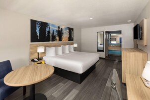 Una habitación de hotel con cama, mesita de noche, lámpara y un cuadro en la pared.