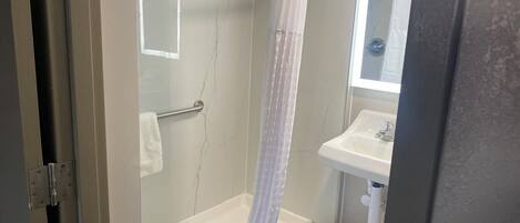 A bathroom with a glass-enclosed shower, a white bathtub, a sink, and a mirror.