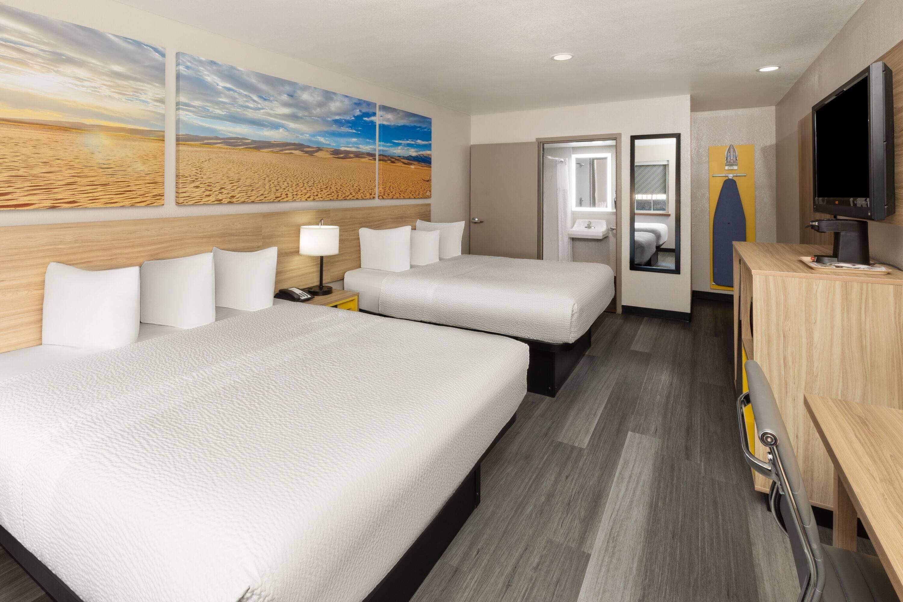 A hotel room with two beds, a TV, a desk, and a bathroom visible through an open door.