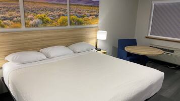 Habitación de hotel con una cama grande, un escritorio con lámpara, una silla y ventana con vista al paisaje desértico.