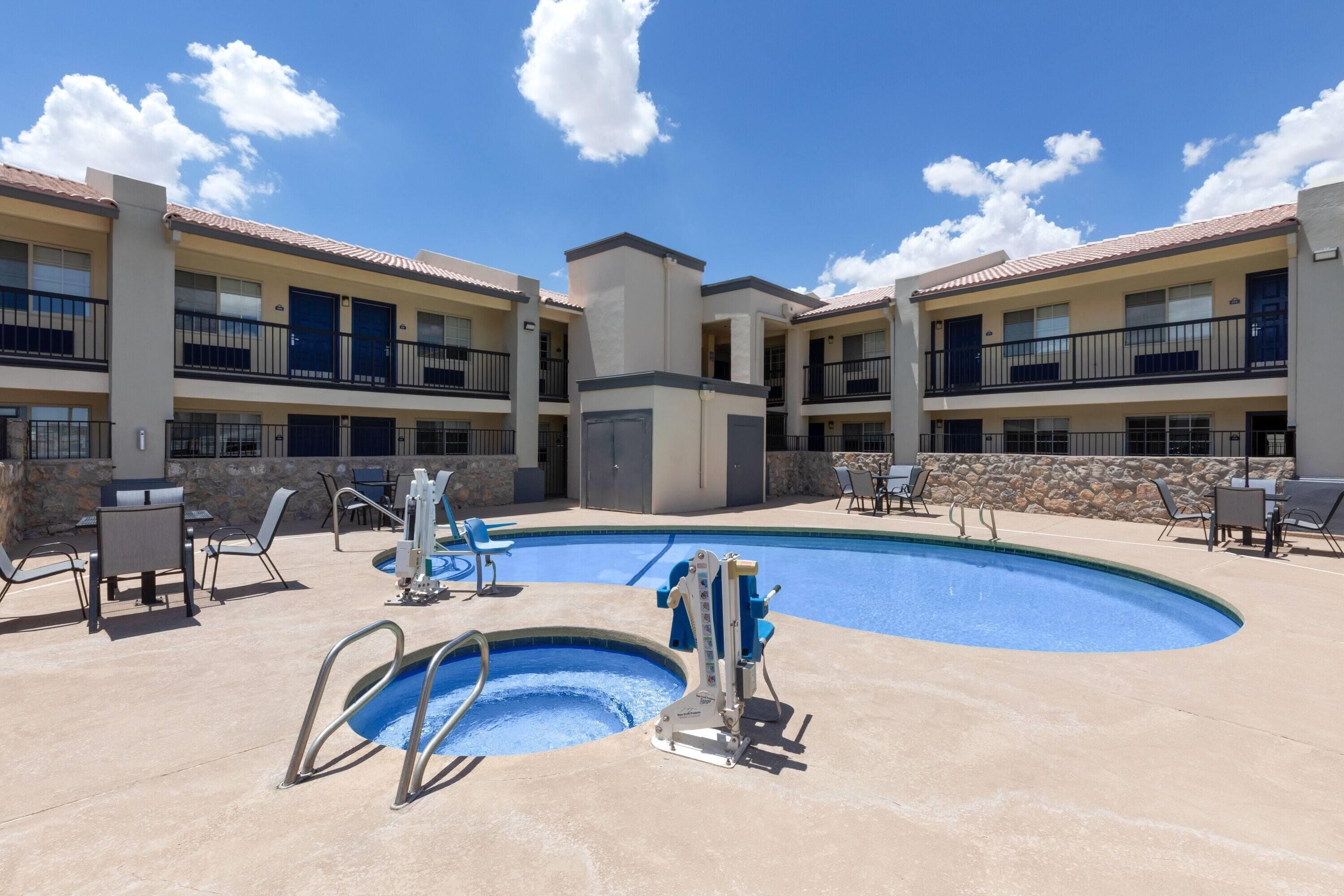 A pool area with a diving board, lounge chairs, and a building with multiple balconies.