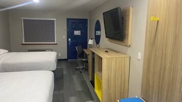 A hotel room with two beds, a desk with a computer, a TV, and a wardrobe.