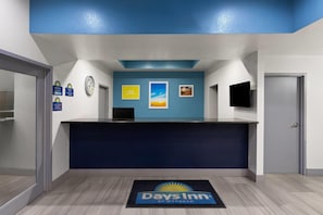 A reception desk with a blue wall, a clock, and a 'Days Inn' doormat.